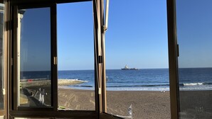 A view from inside a building looking out to a beach with a ship in the distance.
