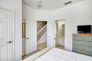 Une chambre à coucher comprenant un lit, une commode, un téléviseur et un escalier menant à une autre pièce.