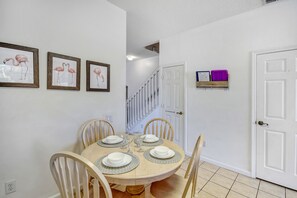 Un coin repas avec une table ronde dressée pour quatre personnes, entourée de chaises en bois. Trois tableaux encadrés sont accrochés au mur au-dessus de la table.