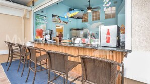 An outdoor bar area with wicker chairs, a counter, and a refrigerator displaying a Coca-Cola logo. - Nature View • King Bed • Pool • 10 minutes to Disney • 5 minutes to shopping (Kissimmee)