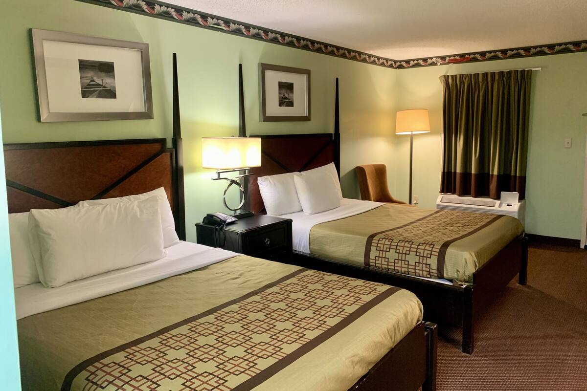 A hotel room with two beds, a nightstand with a lamp, a chair, and a window with curtains.