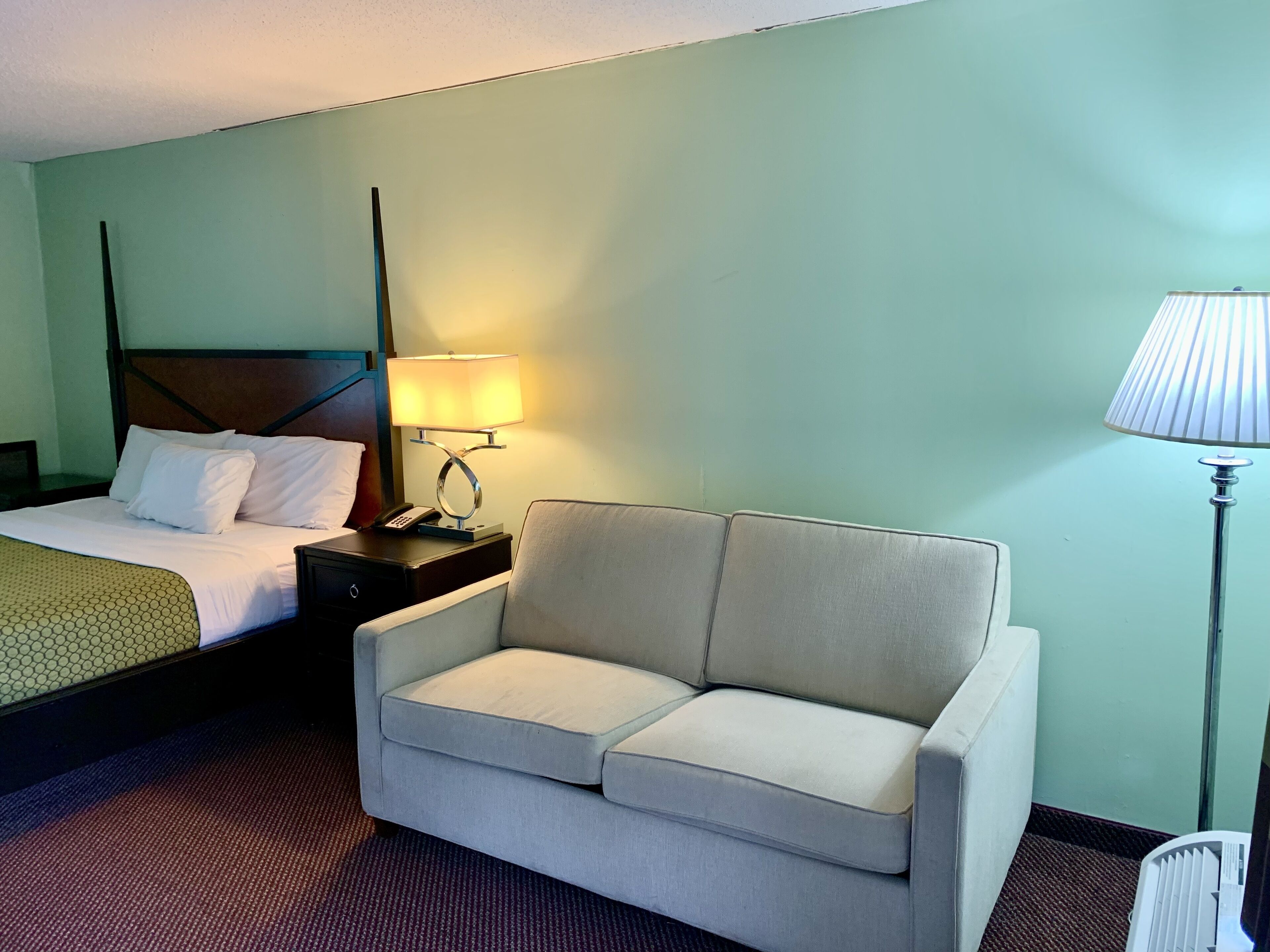 Een hotelkamer met een bed, een nachtkastje met een lamp, een sofa en een vloerbedekking.