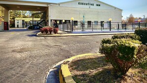 An Executive Inn building with a large parking lot, a covered walkway, and a fenced outdoor area with shrubs. - Executive Inn Chester (Chester)