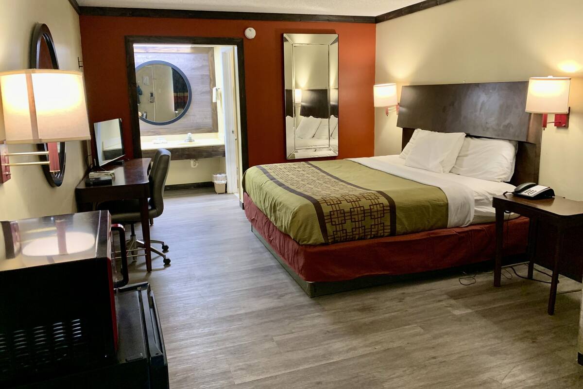 A hotel room with a bed, desk, chair, and a mirror.