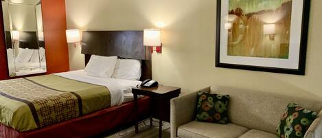Una habitación de hotel con cama, mesita de noche, lámpara y un sofá.