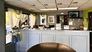 Un espace d'accueil avec un comptoir, une plante, un panneau indiquant la présence d'une connexion Wi-Fi et une vue sur l'extérieur par une fenêtre.