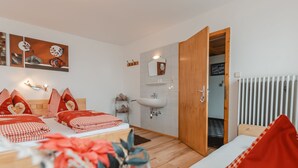 Ein modernes Hotelzimmer mit einem hölzernen Bett, rot-karierter Bettwäsche, einem weißen Waschbecken und Blick auf den Flur.
