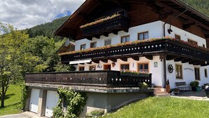 Ein traditionelles Gebäude im alpinen Stil mit einem Blumen geschmückten Balkon und einem Schild mit der Aufschrift 'Taubensteinhof', mit Blick auf einen bewaldeten Berg.