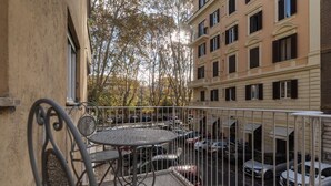 Balcón con sillas y mesas de metal, con vistas a un estacionamiento y edificios cercanos.