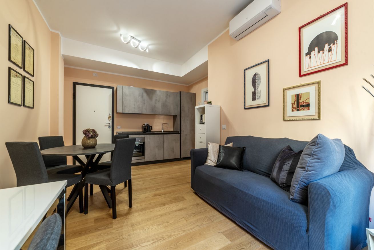 Een moderne woonkamer met een bank, een eettafel, stoelen en een keuken op de achtergrond.