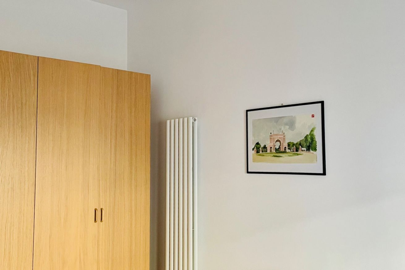 A wooden wardrobe, a radiator, and a framed picture on a wall.