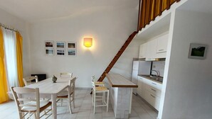 A modern kitchen with white cabinets, a wooden staircase, and a dining area with a white table and chairs. - Gariboldi by Interhome (Palau)