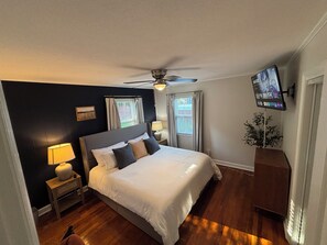 A bedroom with a bed, a ceiling fan, a TV mounted on the wall, and a window with curtains. - 2 bedroom, 1 bath, remodeled 1945 cottage, 1000sq.ft. Two new LUX KING size beds (Siler City)