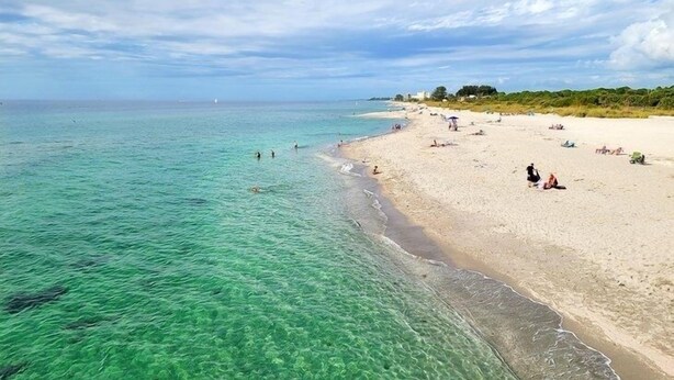 A beach with clear turquoise water, sandy shore, and a few people sunbathing. - Lake Front View, 6 miles from beaches (Nokomis)