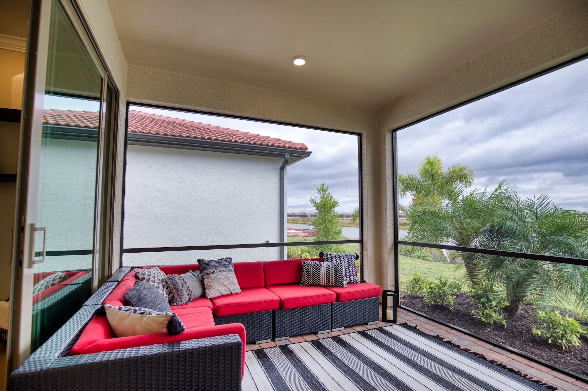 A balcony with a red sofa, a black wicker chair, and a view of a house and greenery.