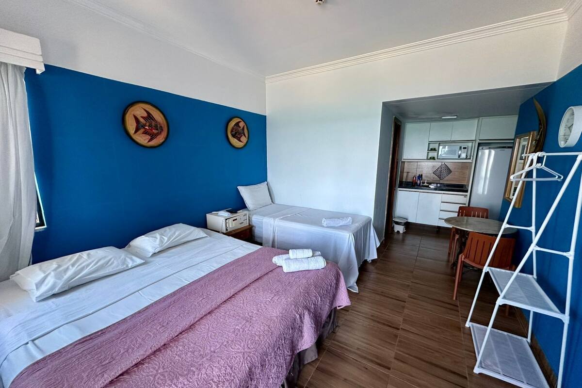 A hotel room with two beds, a kitchenette, and a bathroom visible through an open door.
