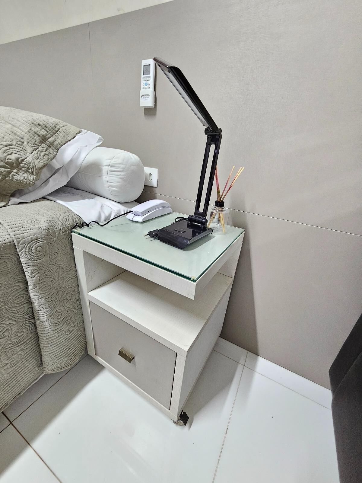 Ein ordentlich eingerichteter Nachttisch mit Lampe, Telefon und einem kleinen Behälter mit Rattan-Diffusor.