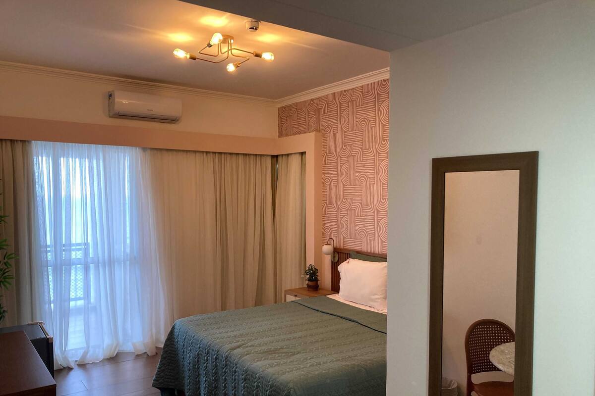 A bedroom with a bed, a desk, a chair, an air conditioner, and a patterned wall.