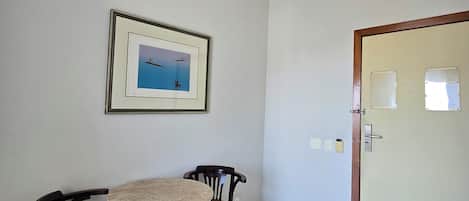 A room with a tiled floor, a round table with two chairs, a framed picture on the wall, and a door with a lock.