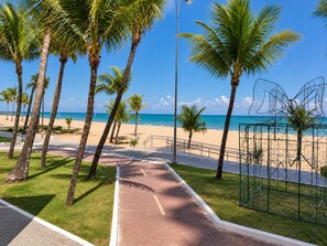 Un sentier pavé mène à une plage bordée de palmiers, sous un ciel bleu et dégagé.