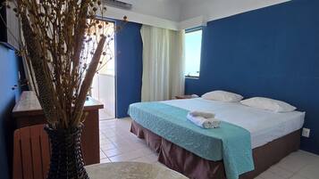 Quarto de hotel com uma cama, uma mesa com um vaso e uma janela com cortinas.