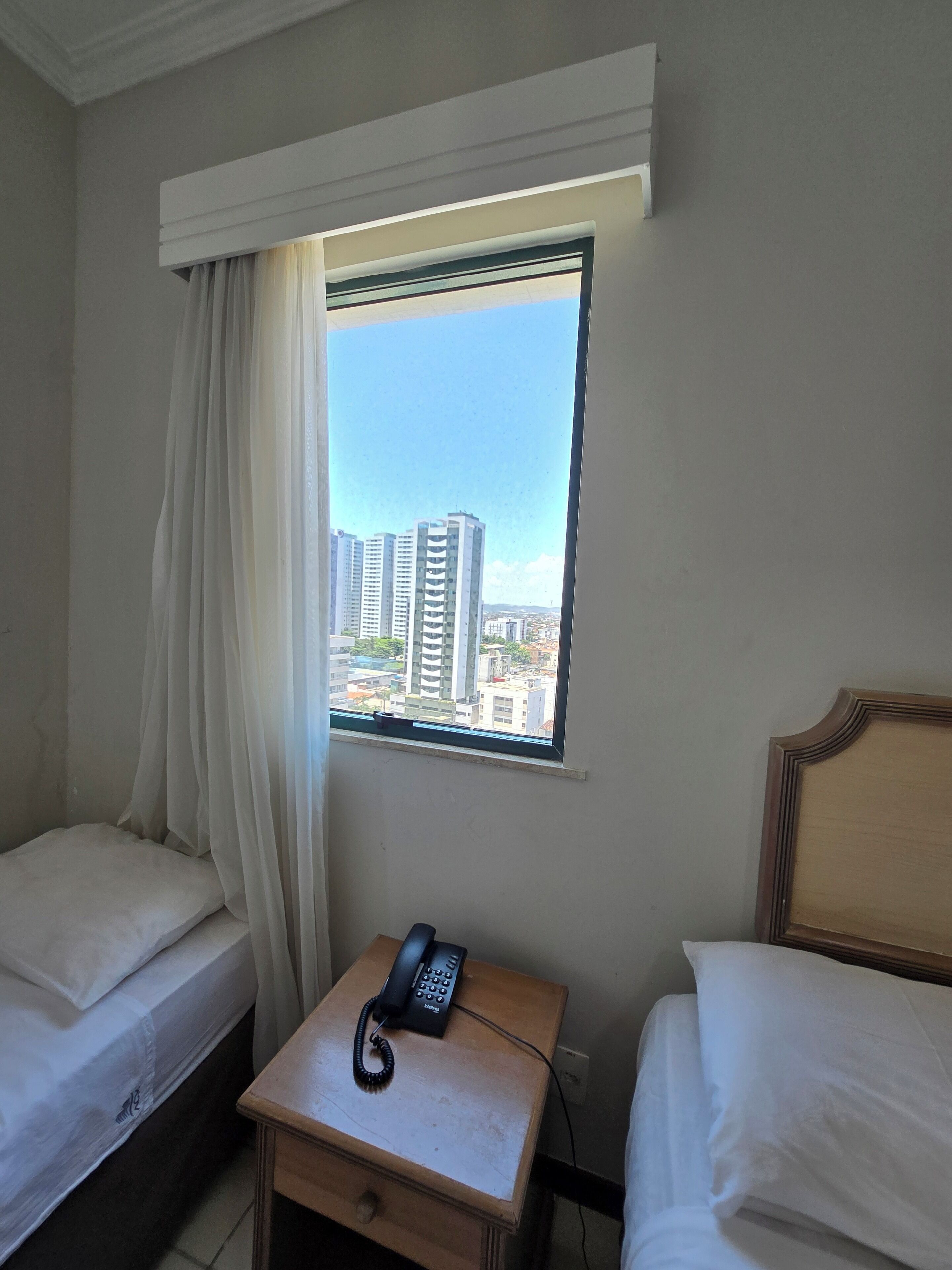 Une chambre d’hôtel avec deux lits, une petite table avec un téléphone et une fenêtre donnant sur la ville.