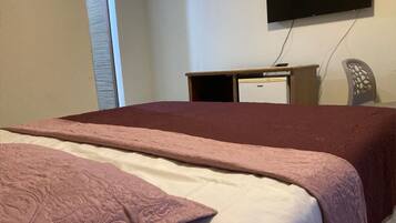 Una habitación con cama, escritorio, silla, televisor y un refrigerador pequeño.