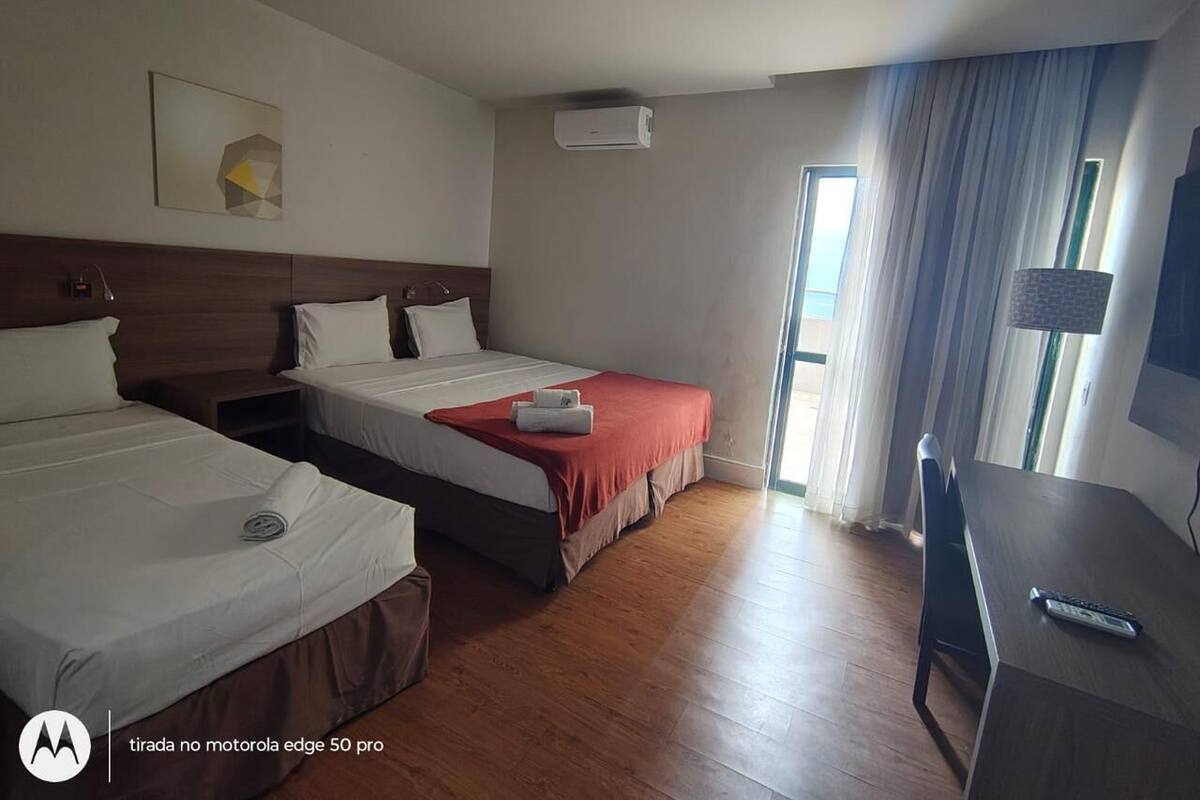 A hotel room with two beds, a desk, and a window with curtains.