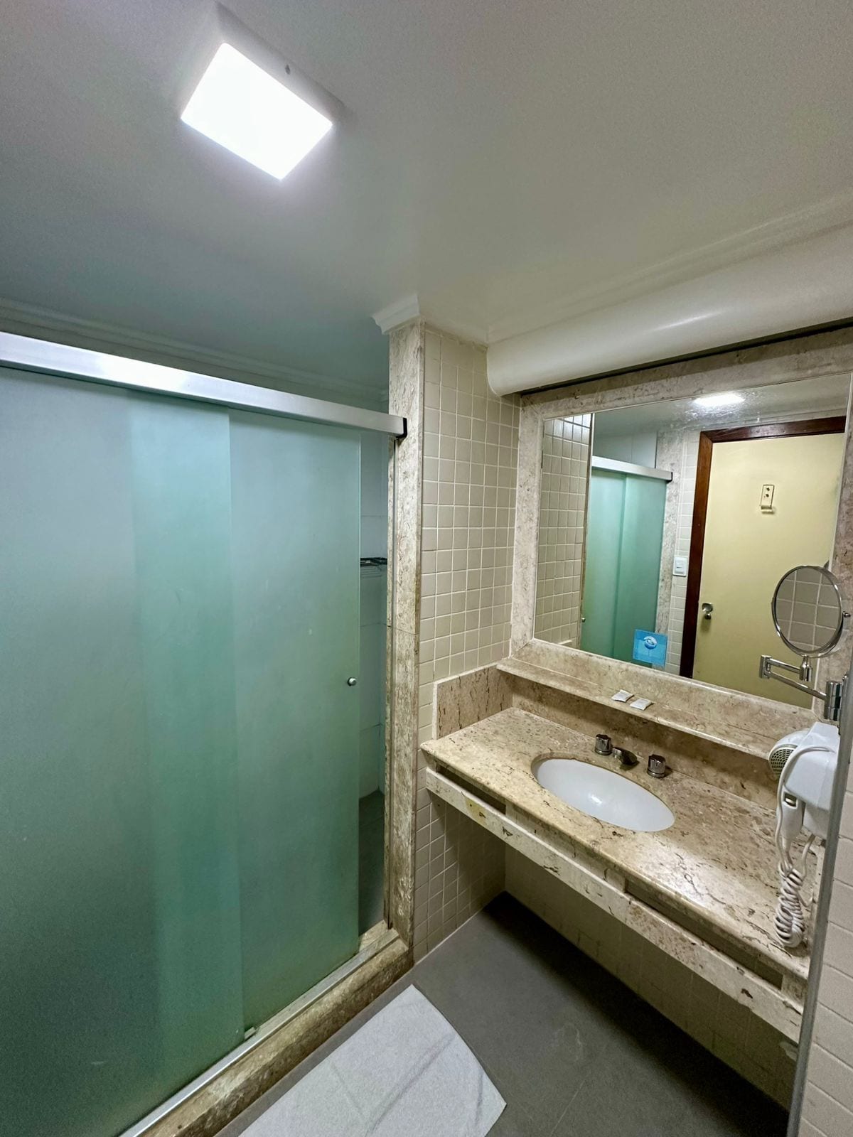 A bathroom with a glass shower enclosure, a sink with a marble countertop, and a mirror.