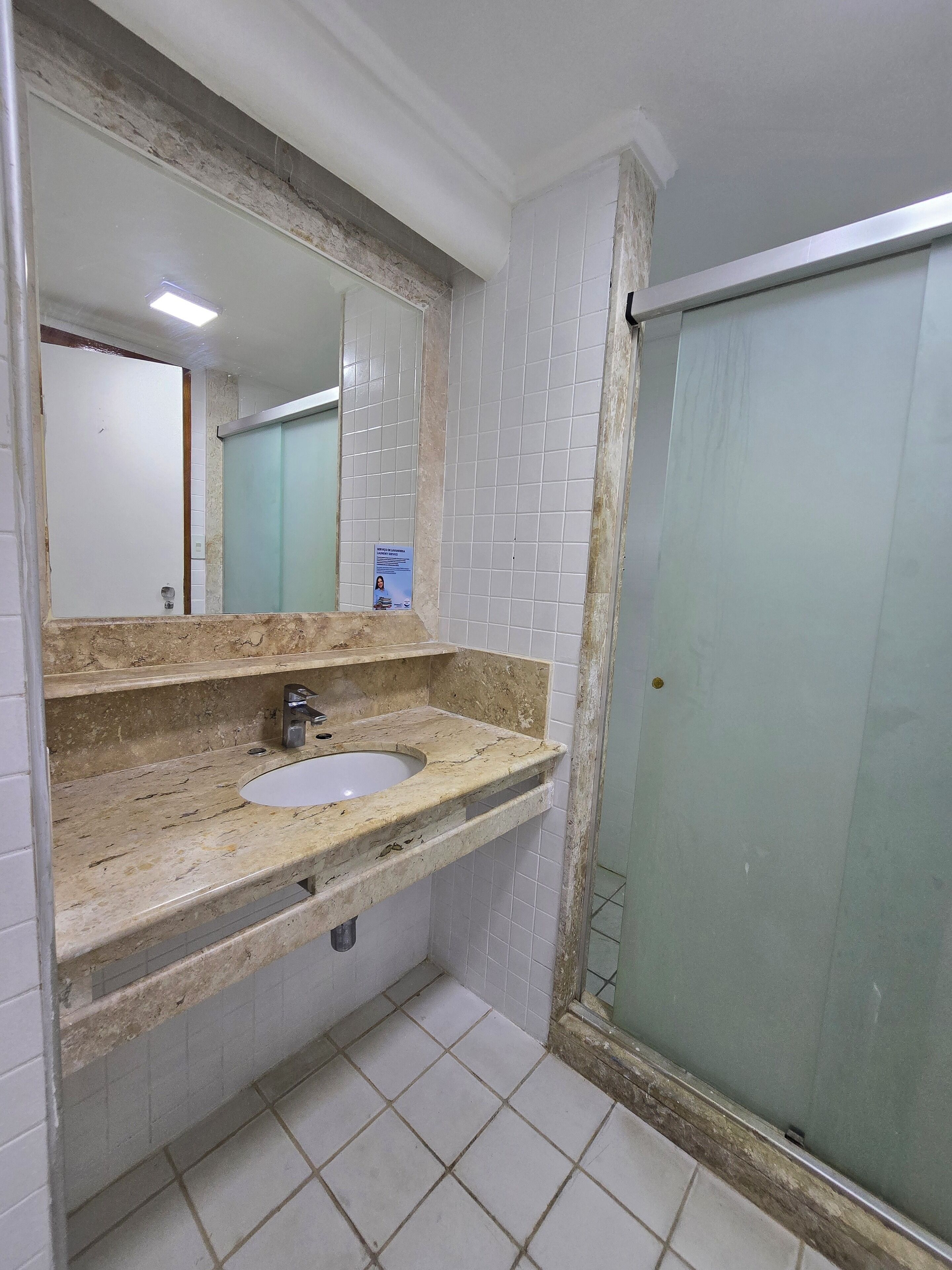 Un baño con lavamanos de mármol, un espejo y una cabina de ducha de vidrio.