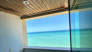 Ein Zimmer mit Holzboden, einem Fenster mit Meerblick und einer Glastür.