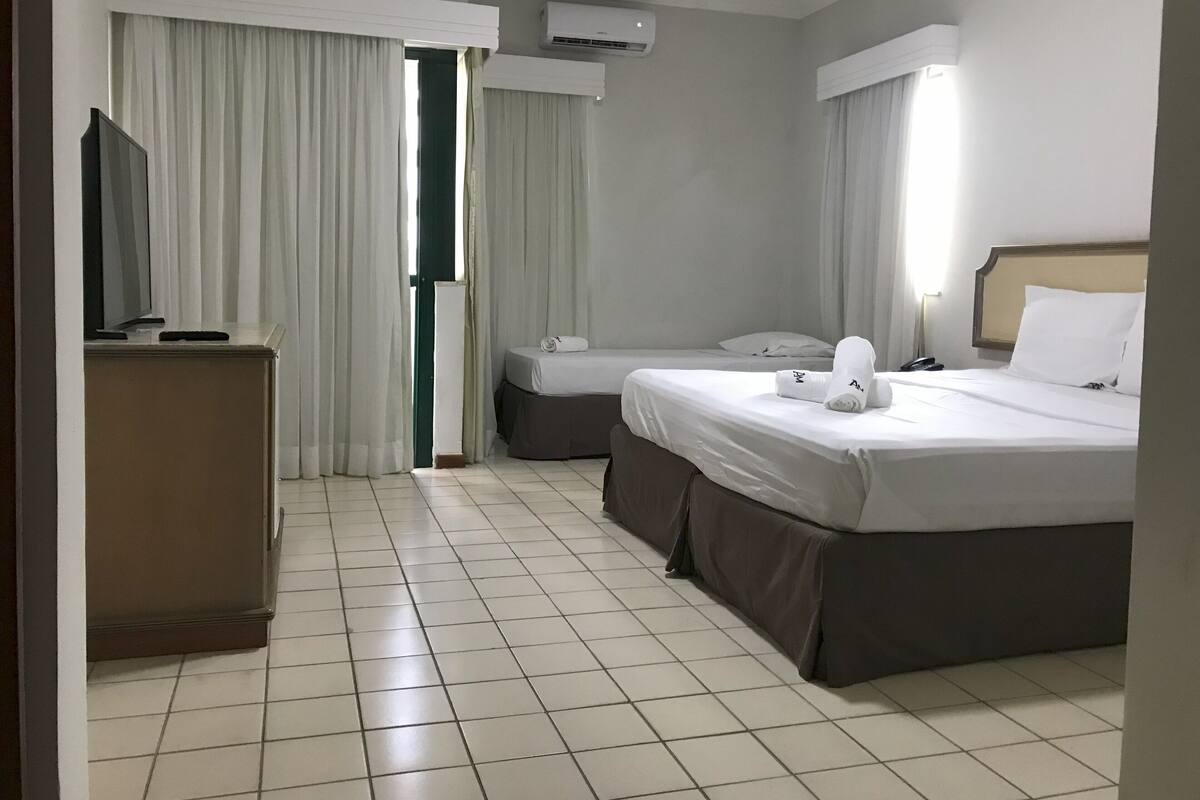 A hotel room with two beds, a desk, and an air conditioning unit.