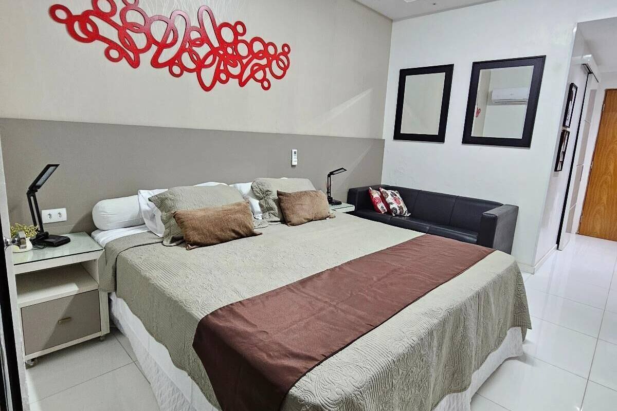 A modern bedroom with a large bed, bedside tables, a wall-mounted air conditioner, and a ceiling light.