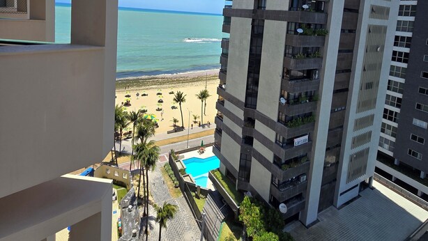 A high-rise building with balconies, a pool, and a beach view.