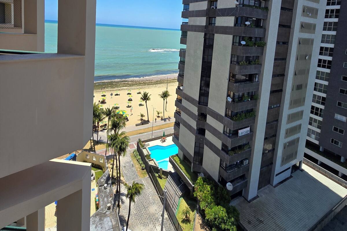A high-rise building with balconies, a pool, and a beach view.