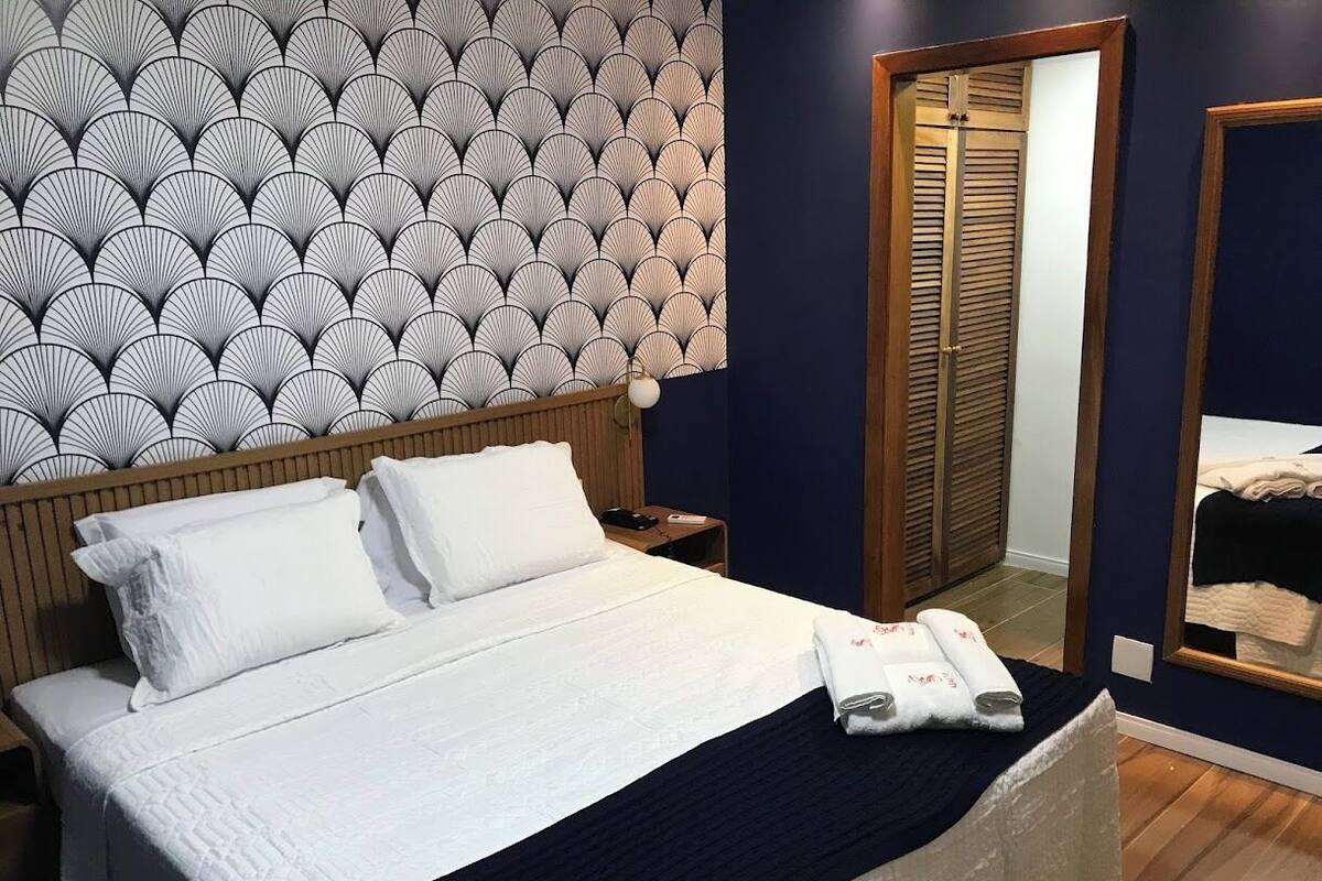 A neatly made bed with white linens, a wooden headboard, and a patterned wallpaper.