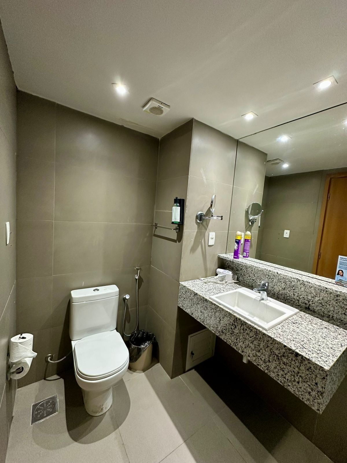 A modern bathroom with a toilet, bidet, and a granite countertop sink with a mirror.