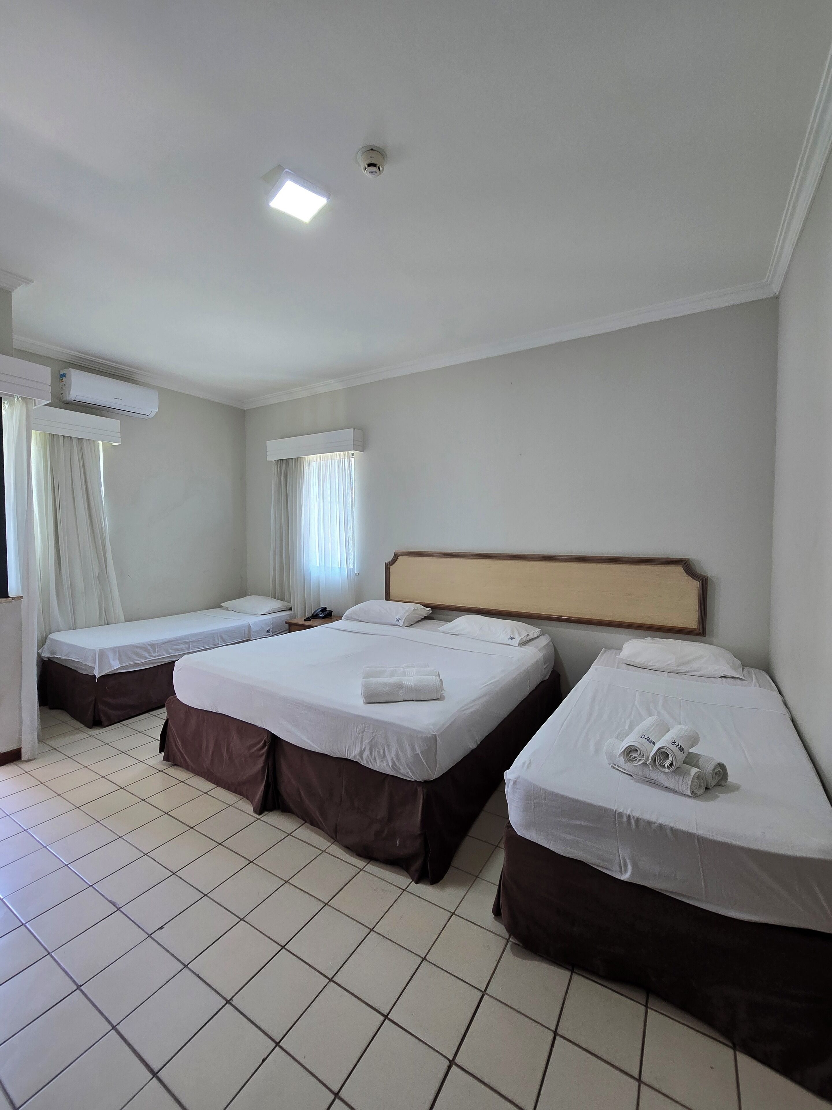 Habitación de hotel con tres camas, un ventilador de techo y una ventana con cortinas.