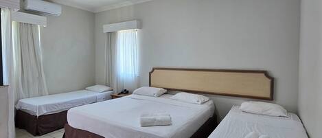 Habitación de hotel con tres camas, un ventilador de techo y una ventana con cortinas.
