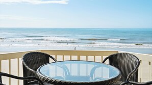 Een balkon met rieten stoelen en een glazen tafel, met uitzicht op de oceaan.