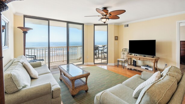 Een woonkamer met een bank, een salontafel, een televisie en een balkon met uitzicht op de oceaan.
