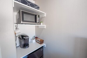 Uma cozinha compacta com micro-ondas, cafeteira e prateleiras para armazenamento.