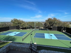 An outdoor tennis court with a stone wall and trees in the background. - Hill Country getaway at Barton Creek Lakeside near Lakecliff Golf Club. (Spicewood)