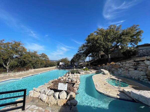 A pool area with clear blue water, stone walls, and a sign warning against climbing on rocks. - Hill Country getaway at Barton Creek Lakeside near Lakecliff Golf Club. (Spicewood)