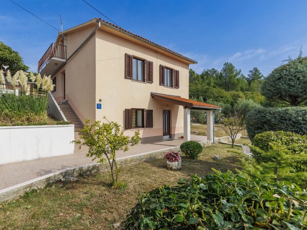 Une maison à deux étages avec un balcon, un petit jardin et une allée pavée.