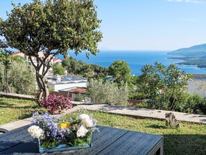 Uma mesa com um vaso de flores, uma árvore e vista para o mar e prédios.