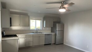 A kitchen with white cabinets, a stainless steel refrigerator, a dishwasher, and a ceiling fan. - New, Fun-Size Benbow House! (Garberville)