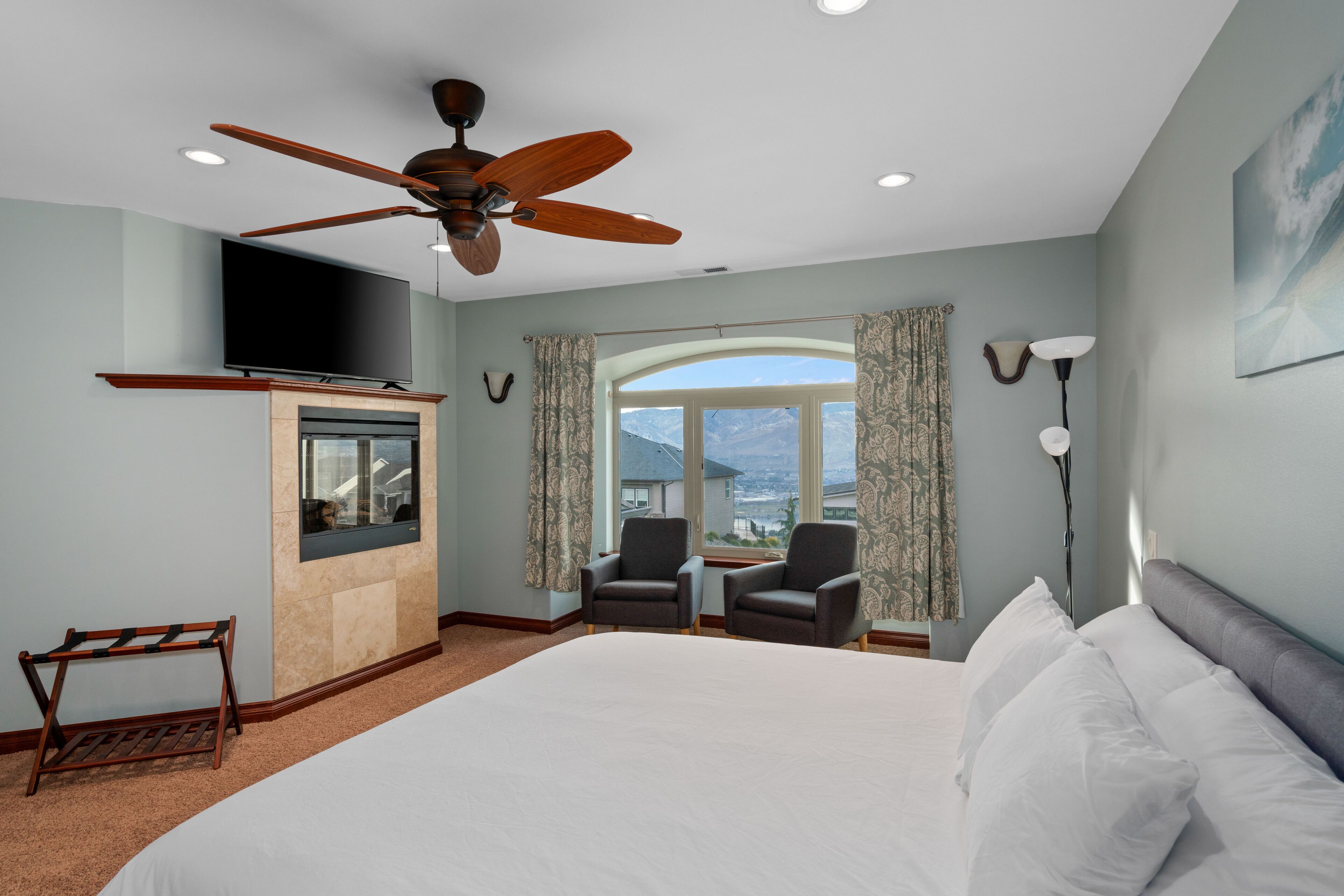 Ein Hotelzimmer mit einem großen Bett, einem Deckenventilator, einem Fernseher, einem Kamin, zwei Sesseln, einem kleinen Tisch und einem Fenster mit Bergblick.