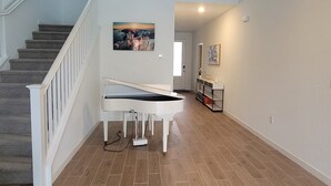 A spacious hallway with a piano, a staircase, and a door leading to another room. - Sequoia Deluxe / Brand New 5 beds/ 3.5 baths  (Visalia)
