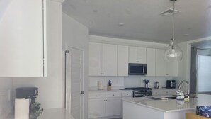 A modern kitchen with white cabinetry, a central island, a microwave, stove, and a hanging pendant light. - Sequoia Deluxe / Brand New 5 beds/ 3.5 baths  (Visalia)
